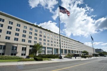 Tall building with windows behind a waving American flag on a sunny day