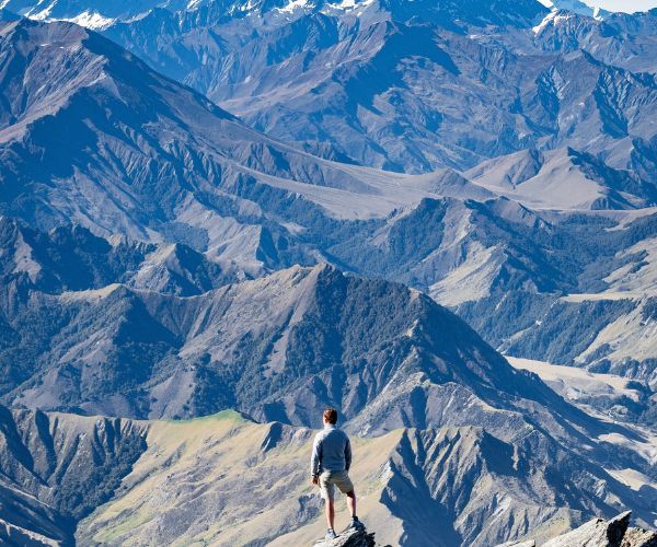 A man standing on a mountaintop looking out over a range of mountains