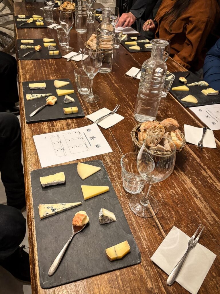 Wine and cheese tasting at Paroles de Fromagers, featuring a variety of French cheeses on a rustic table with wine glasses and tasting cards.