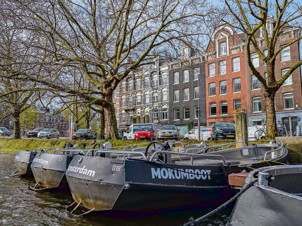 A fleet of Mokumboot rental boats line the serene canal of Amsterdam