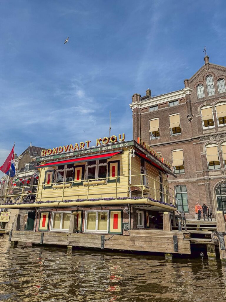 Experience the Rondvaart Koou boat trip on the iconic canals of Amsterdam with Dutch architecture and clear blue skies.